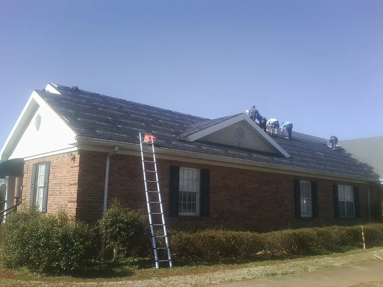 Crew tearing shingles off a brick ranch roof with a ladder set — Emergency Roof Repair work by our crew in Hopatcong