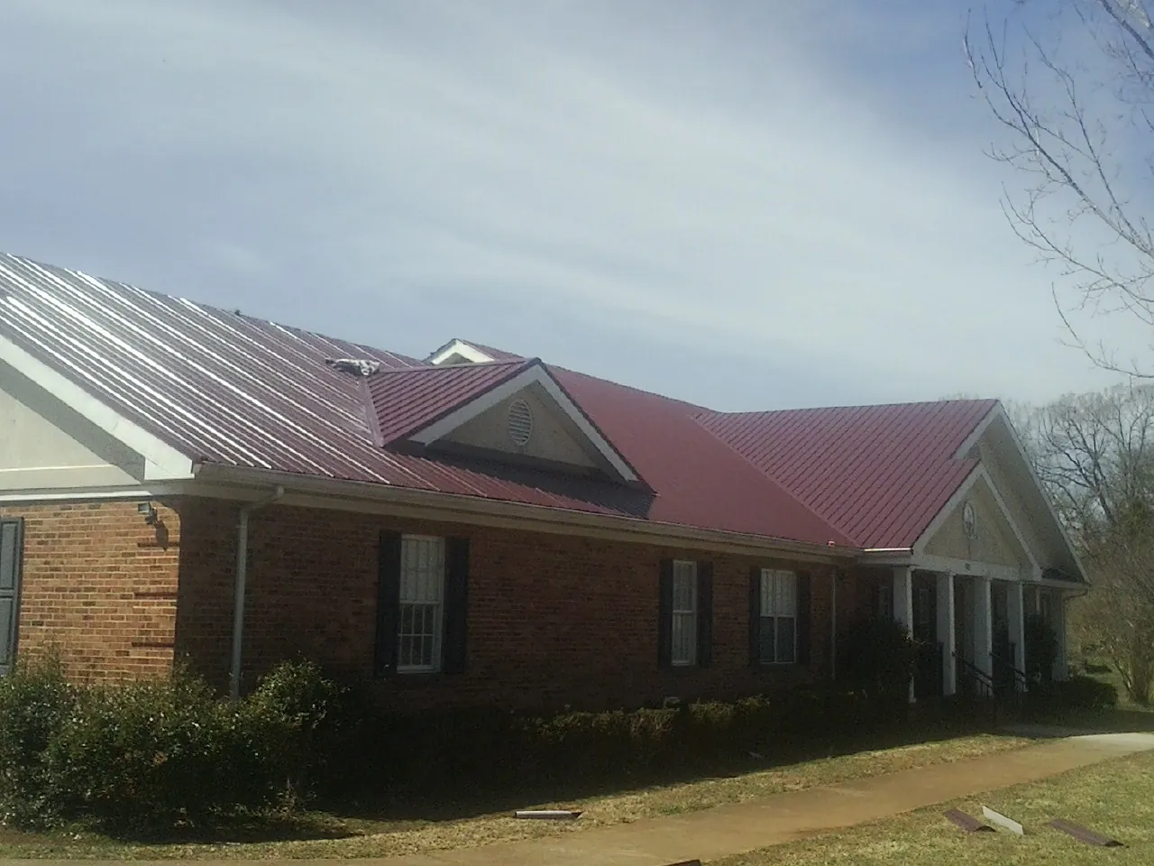 Red metal roof with gabled entries on a long brick building, from a Hail Damage Roof Repair job in Hopatcong
