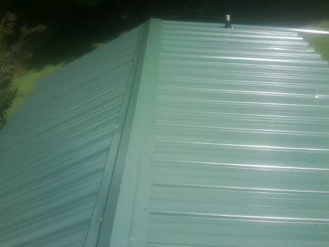 New green metal panels meeting at the ridge of a roof — Flat Roof Repair work by our crew in Hopatcong
