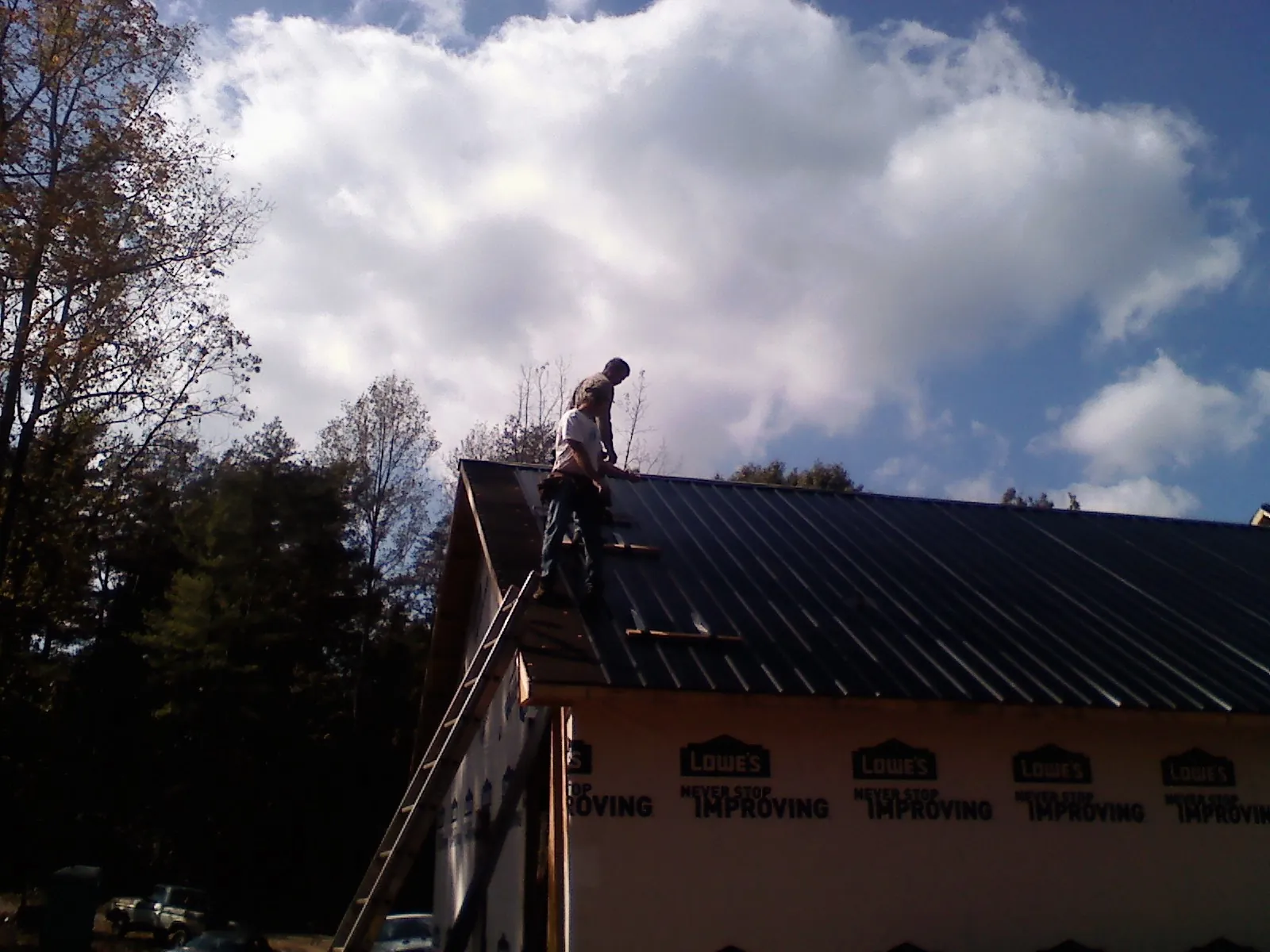 Roofer fastening dark metal panels high against a cloudy sky, from a Roof Inspection job in Hopatcong