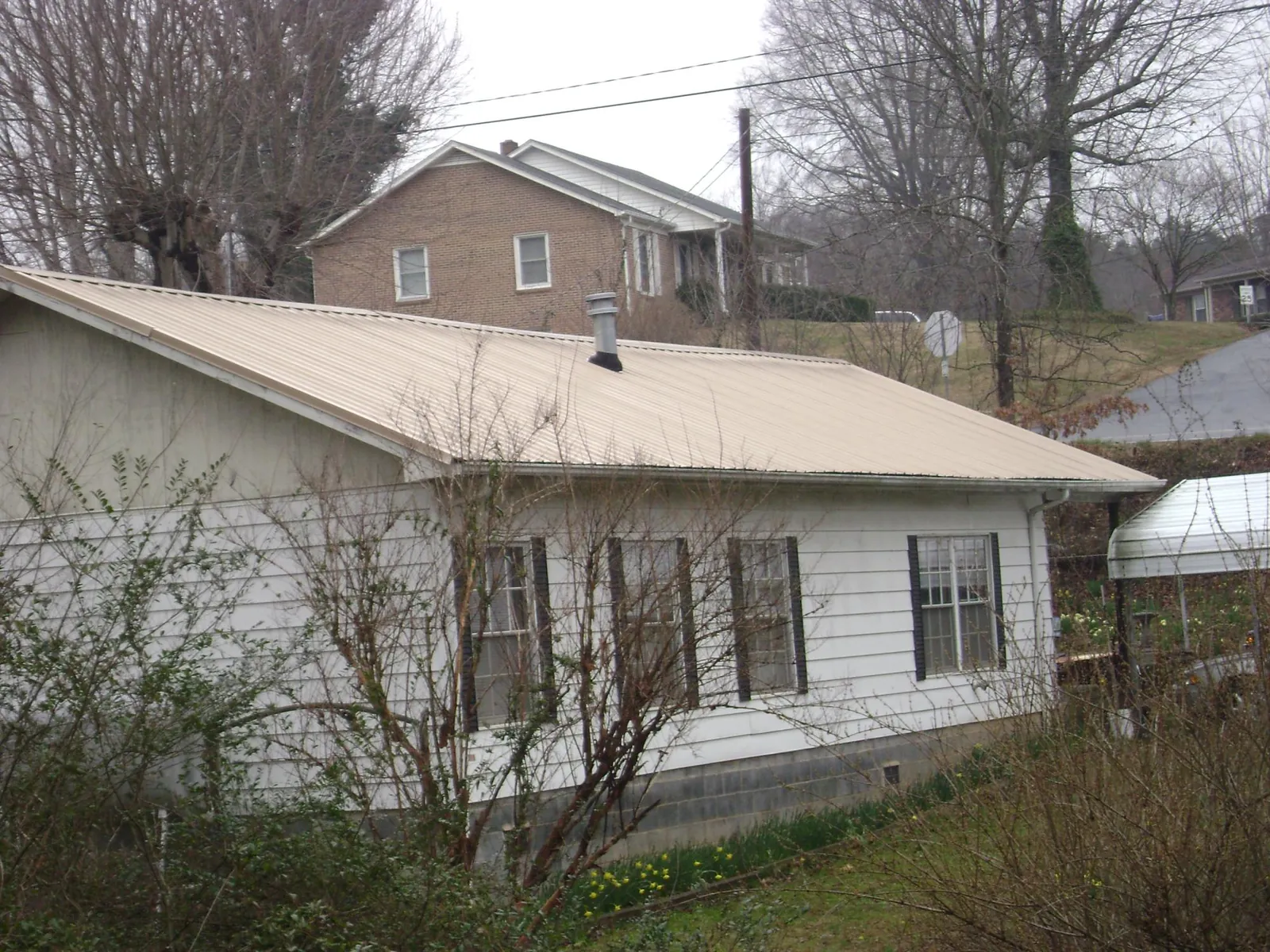 Tan metal roof on a white sided house set into a hillside — Commercial Roofing by Roofing Brothers in Hopatcong